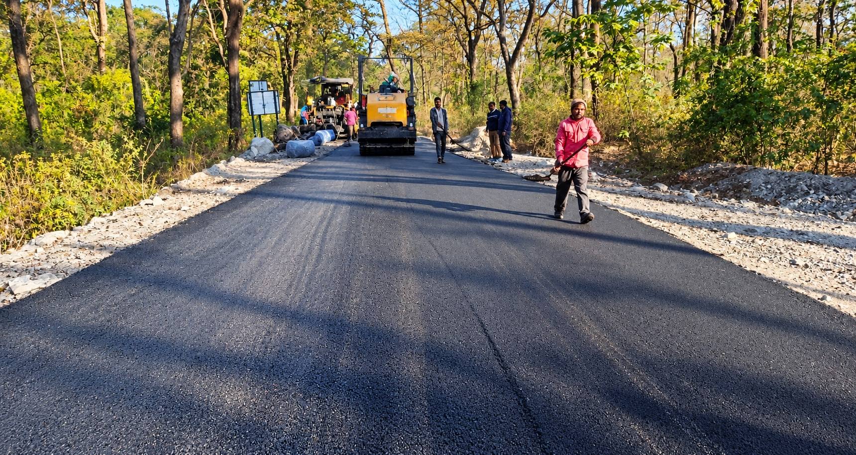 Freshly laid bituminous road surface with a paver and crew working behind
