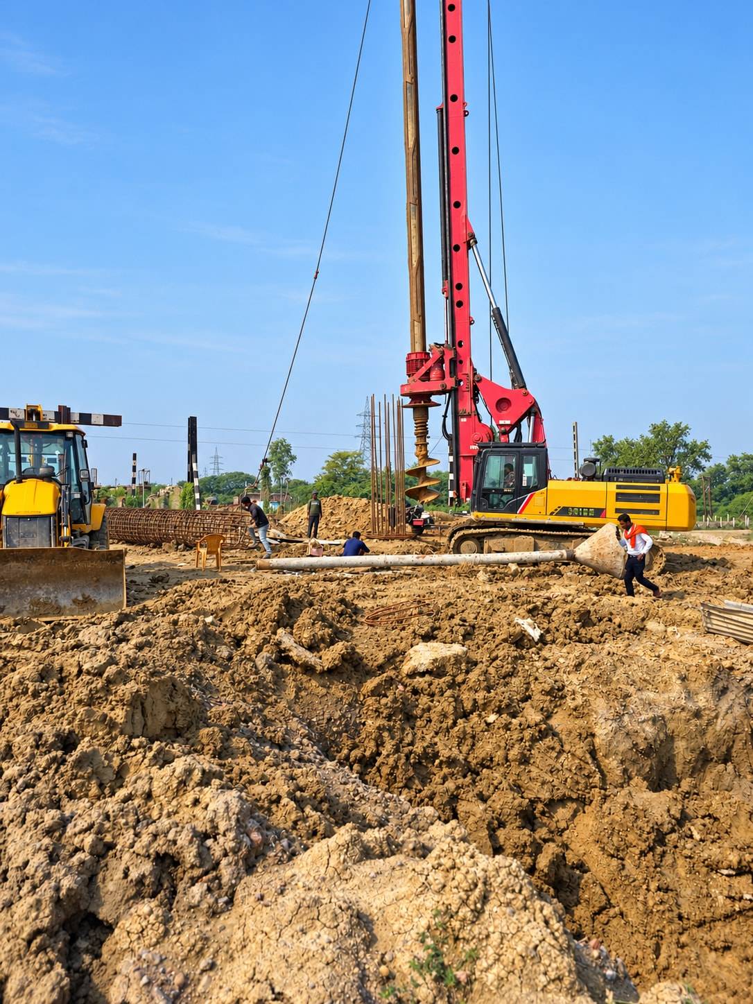 Rotary piling rig and backhoe loader on an excavated foundation site