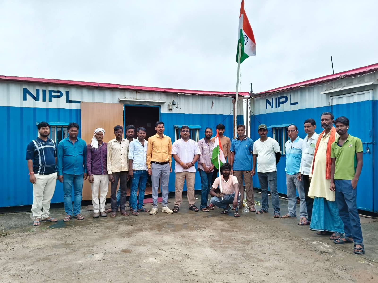 The NIPL site team standing in front of the NIPL site office, with the national flag raised